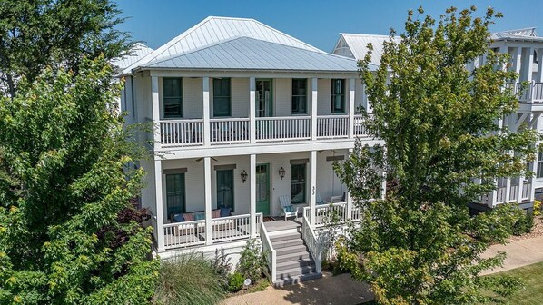 A two-story white building with a balcony on the second floor, surrounded by trees.
