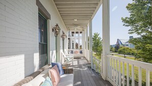 Eine überdachte Veranda mit weißem Geländer, einer Bank mit Kissen und Blick auf ein Gebäude im Hintergrund.