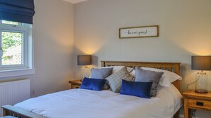 Un dormitorio ordenado con cama, mesitas de noche y una ventana con cortinas.