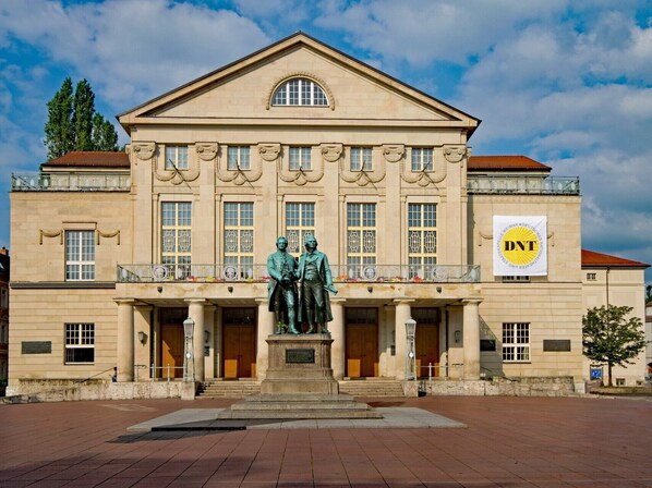 A stately building with a classical facade, featuring a central statue, large windows, and a prominent banner.