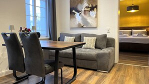 A modern hotel room with a dining area, a gray sofa with patterned cushions, a wooden dining table, and a large abstract painting on the wall. - Modern holiday flat with comfortable furnishings, quiet and centrally located (Weimar)