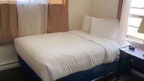 Ett hotellrum med en stor säng, ett nattduksbord, en lampa och tunna, genomskinliga gardiner.