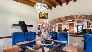 A dining area with a glass table, blue upholstered chairs, and a cross on the wall. - +MS +Casa Tequis +Hermoso Jardín (Tequisquiapan)