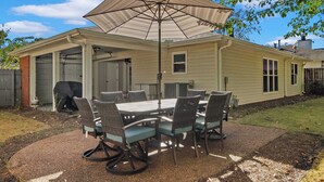 A covered patio with a table and chairs, a large umbrella, and a brick wall.