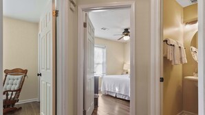 A hallway leading to a bedroom with a bed, a chair, and a bathroom with a sink and towels.