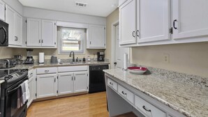 A modern kitchen with white cabinets, a granite countertop, a red bowl, and a window with blinds.