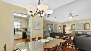 A spacious living area with a glass dining table, wooden chairs, a grey sofa, and a ceiling fan.