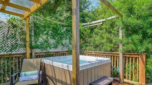 Eine Holzterrasse mit Whirlpool, überdachter Sitzgelegenheit und einem Spalierzaun.