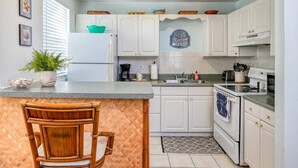 A kitchen with white cabinets, a wooden chair, a coffee maker, and a toaster. - Vilano Cottage Unit B (St. Augustine)