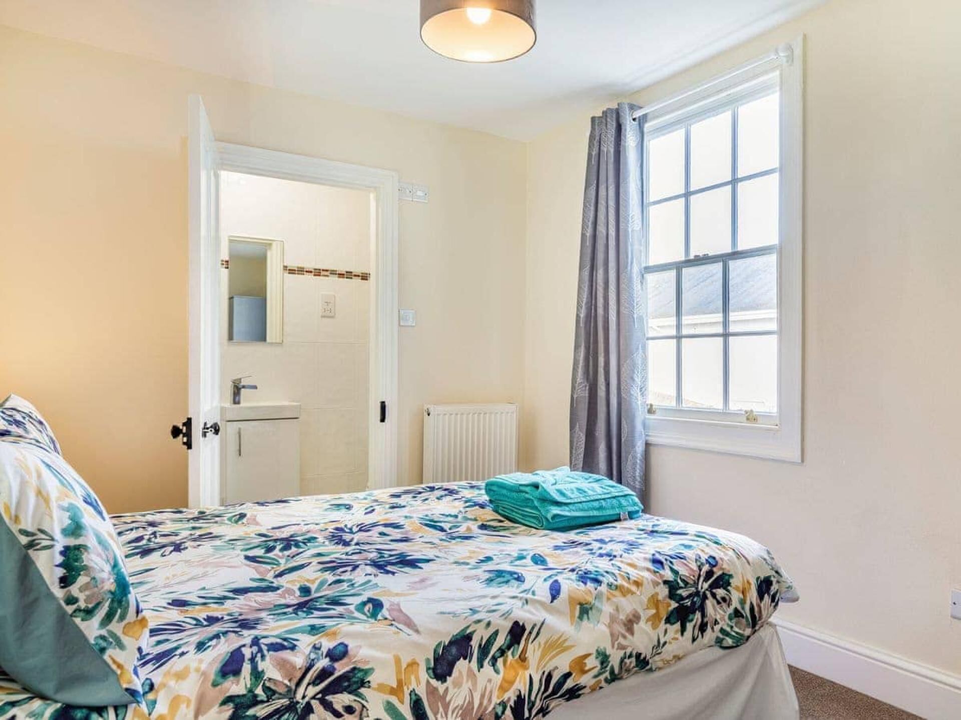 Une chambre à coucher avec un lit, une fenêtre avec des rideaux, un radiateur et une porte donnant sur une autre pièce.