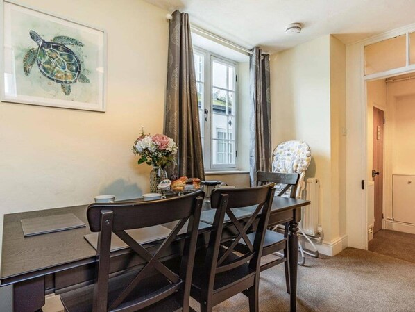 Un comedor con una mesa y sillas, un jarrón con flores y una ventana con cortinas.