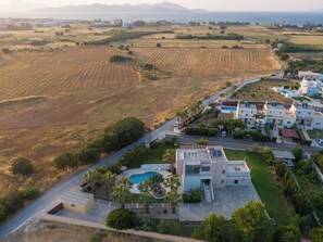 Vista aérea de uma área residencial costeira com casas modernas, piscina e campos agrícolas.