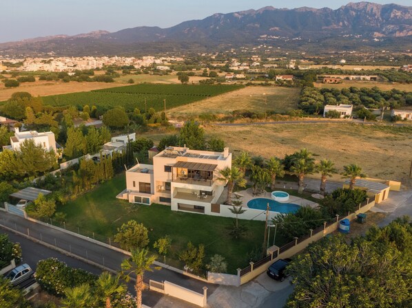 A modern two-story house with a swimming pool, surrounded by a well-maintained lawn and palm trees.