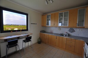 A kitchen with wooden cabinets, a window with a view, a countertop, and two bar stools.