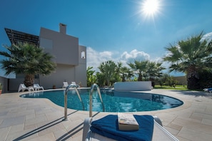 A swimming pool with lounge chairs, a modern building, and palm trees.