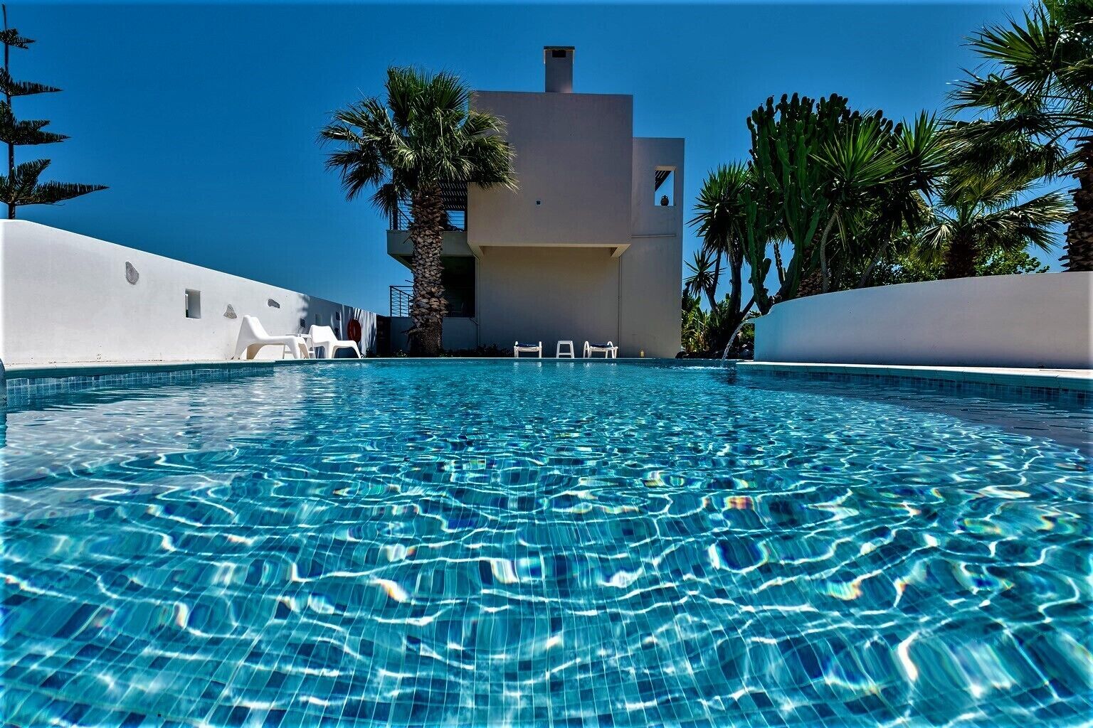 Une piscine d’un bleu éclatant, avec un bâtiment moderne en arrière-plan, le tout entouré de palmiers.