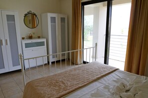 Quarto com uma cama, guarda-roupa, espelho e vista através de uma porta de vidro.