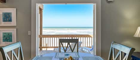 A dining area with a view of the ocean, wooden ceiling beams, and framed pictures on the wall.