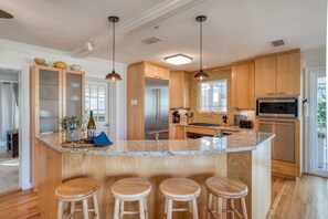 Uma cozinha moderna com ilha central, banquetas de madeira, eletrodomésticos de aço inoxidável e iluminação pendente.