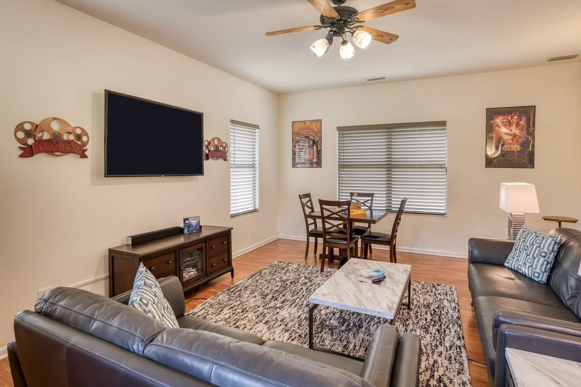 A living room with a flat-screen TV, a ceiling fan, a dining area with a table and chairs, and a sofa.