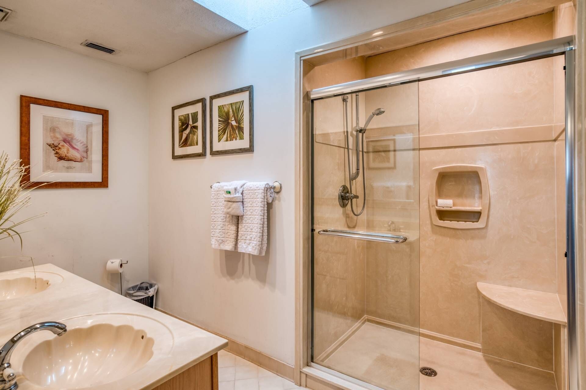 Une salle de bain moderne avec une douche à parois de verre, un grand lavabo et des œuvres d’art encadrées accrochées au mur.