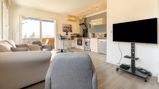 Un salon moderne avec un canapé, un fauteuil gris et un téléviseur fixé au mur.
