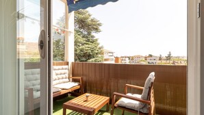 Un balcon avec une table en bois, deux chaises rembourrées et une vue sur les immeubles et les arbres.