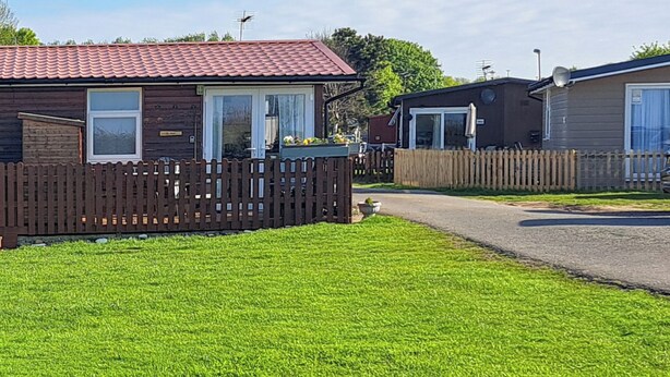 A row of mobile homes with a wooden fence in front, a paved driveway, and a grassy area.