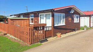A wooden mobile home with a red roof, a fenced yard, and a satellite dish.
