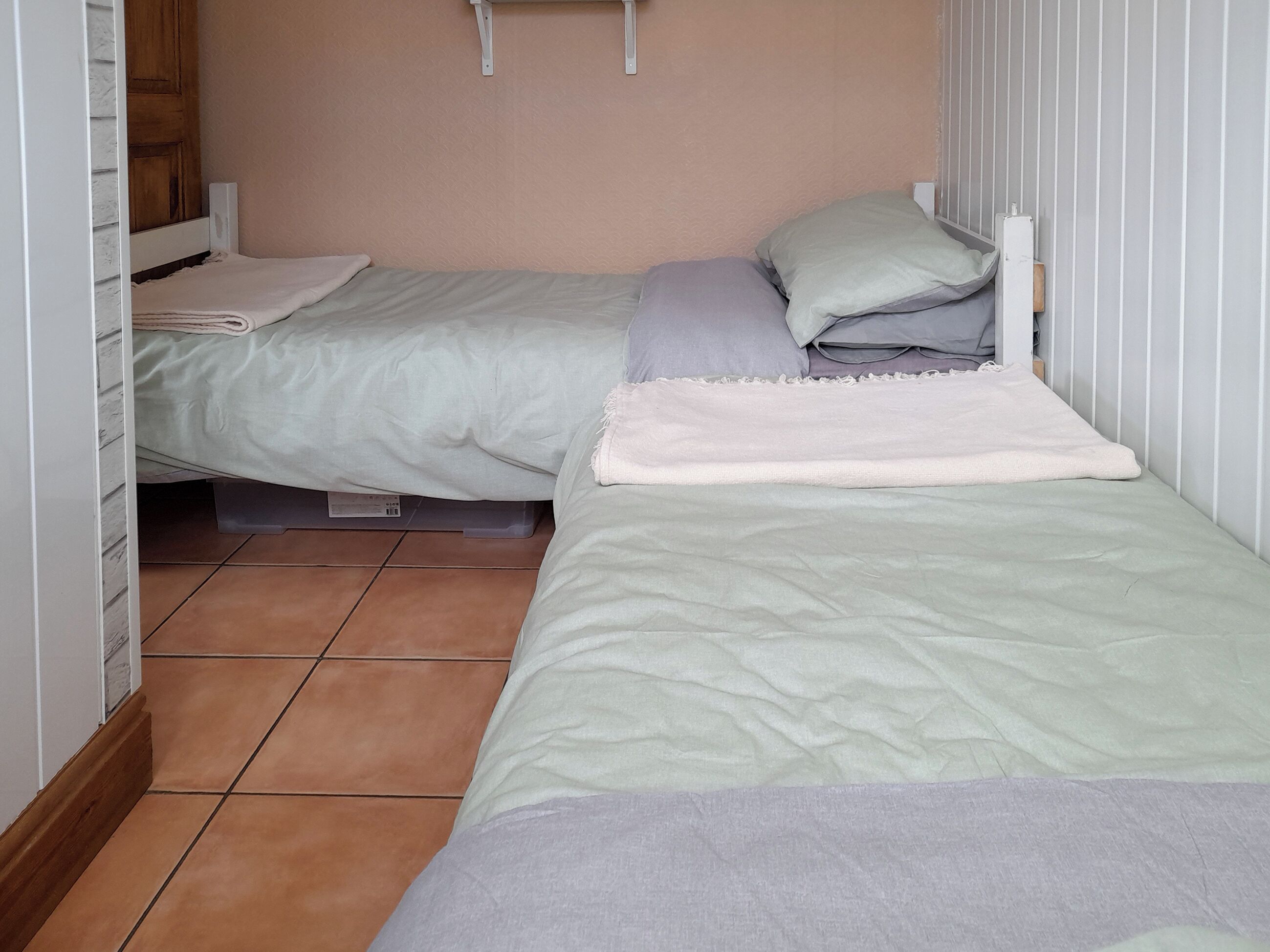 A small, neatly arranged bedroom with two single beds, each with a pillow and a blanket.
