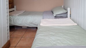 A small, neatly arranged bedroom with two single beds, each with a pillow and a blanket.
