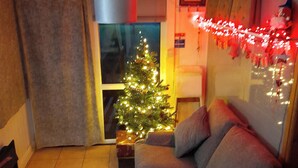 A cozy living room with a grey sofa, a small Christmas tree, and a glass table with two wine glasses.