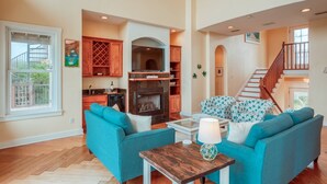 A spacious living room with a fireplace, a kitchen area with wooden cabinets, and a staircase leading to an upper level. - Tuckers Hideaway at Seagate (St. Augustine)