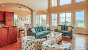 A spacious living area with a kitchen, two sofas, a coffee table, and large windows offering a view of the outdoors. - Tuckers Hideaway at Seagate (St. Augustine)