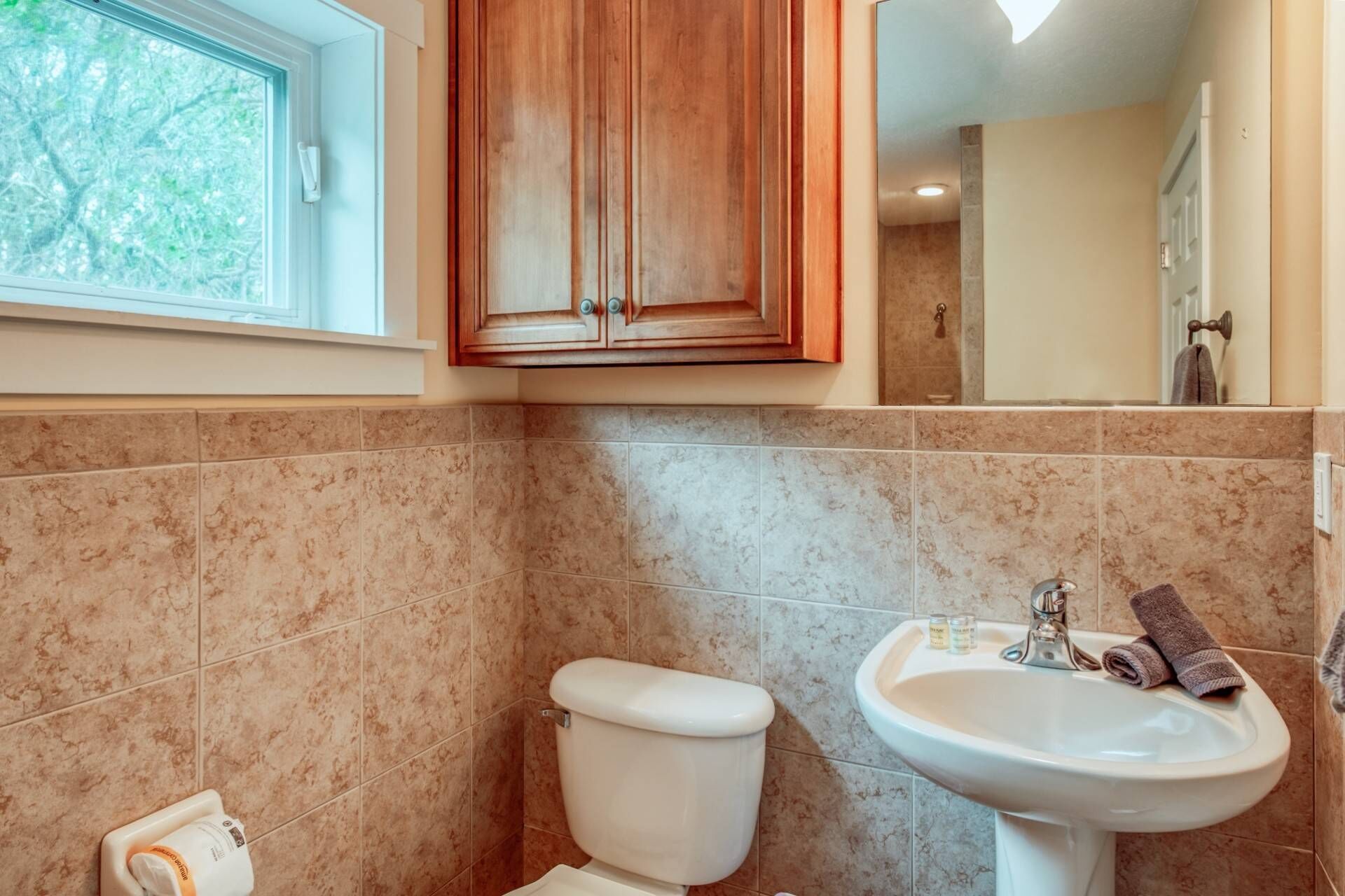 A bathroom with a toilet, sink, and wooden cabinet.