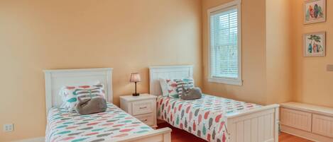 A bedroom with two beds, a nightstand, a window with blinds, and artwork on the wall.