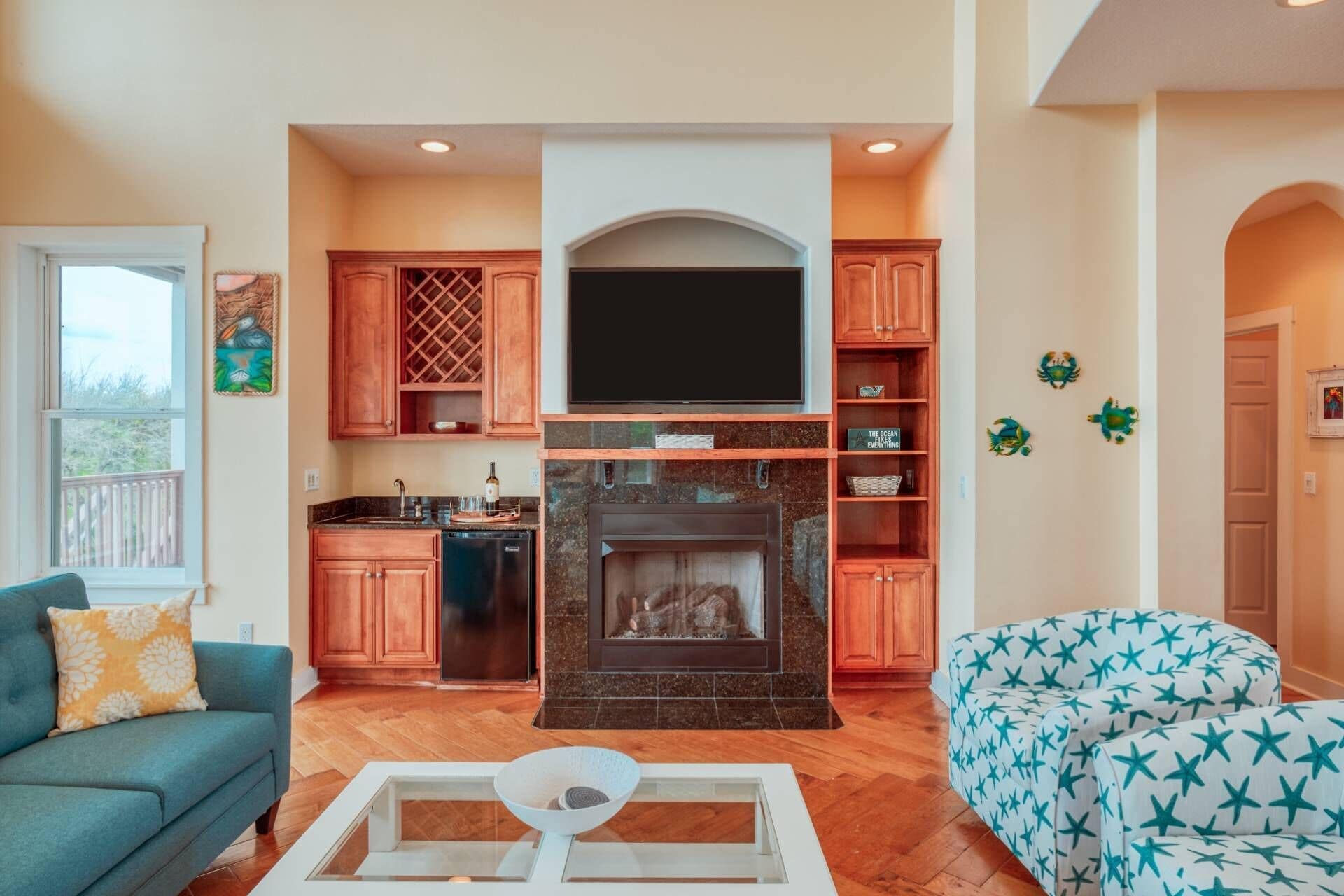 A living room with a fireplace, a television, and a kitchen area with wooden cabinets and a stone backsplash.