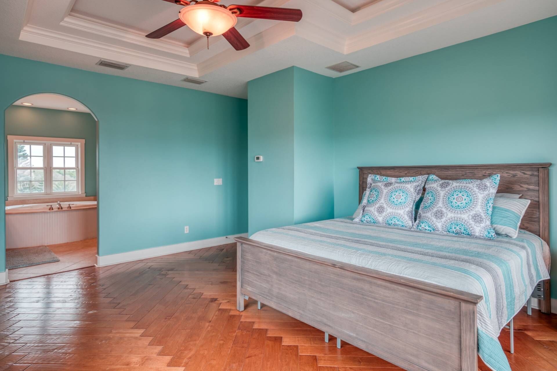 Un dormitorio con cama de madera, paredes color turquesa y ventilador de techo.