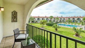 A balcony with wicker furniture, a view of a pool, and a building with red-tiled roofs. - Ocean Club 38 (St. Augustine)