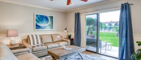 A living room with a beige sofa, a coffee table, and a large window with blue curtains.