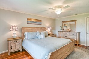 Une chambre à coucher avec un lit en bois, deux tables de chevet avec des lampes, un ventilateur de plafond et un grand miroir au-dessus d’une commode.