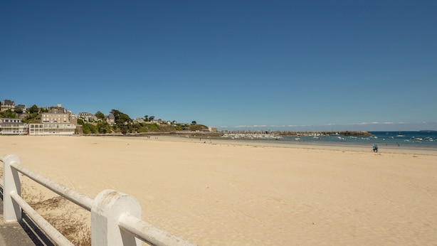 Ein breiter, sandiger Strand mit einer weißen Brüstung im Vordergrund.