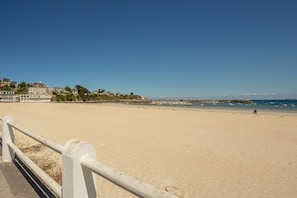 A wide sandy beach with a white railing in the foreground.