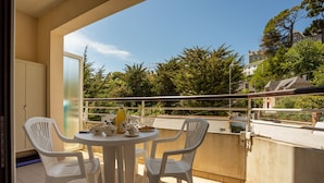 Ein Balkon mit rundem Tisch und vier weißen Stühlen, mit Blick auf eine Wohngegend mit Bäumen und Häusern.