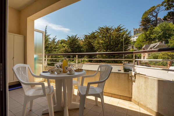 A balcony with a round table and four white chairs, overlooking a residential area with trees and houses.