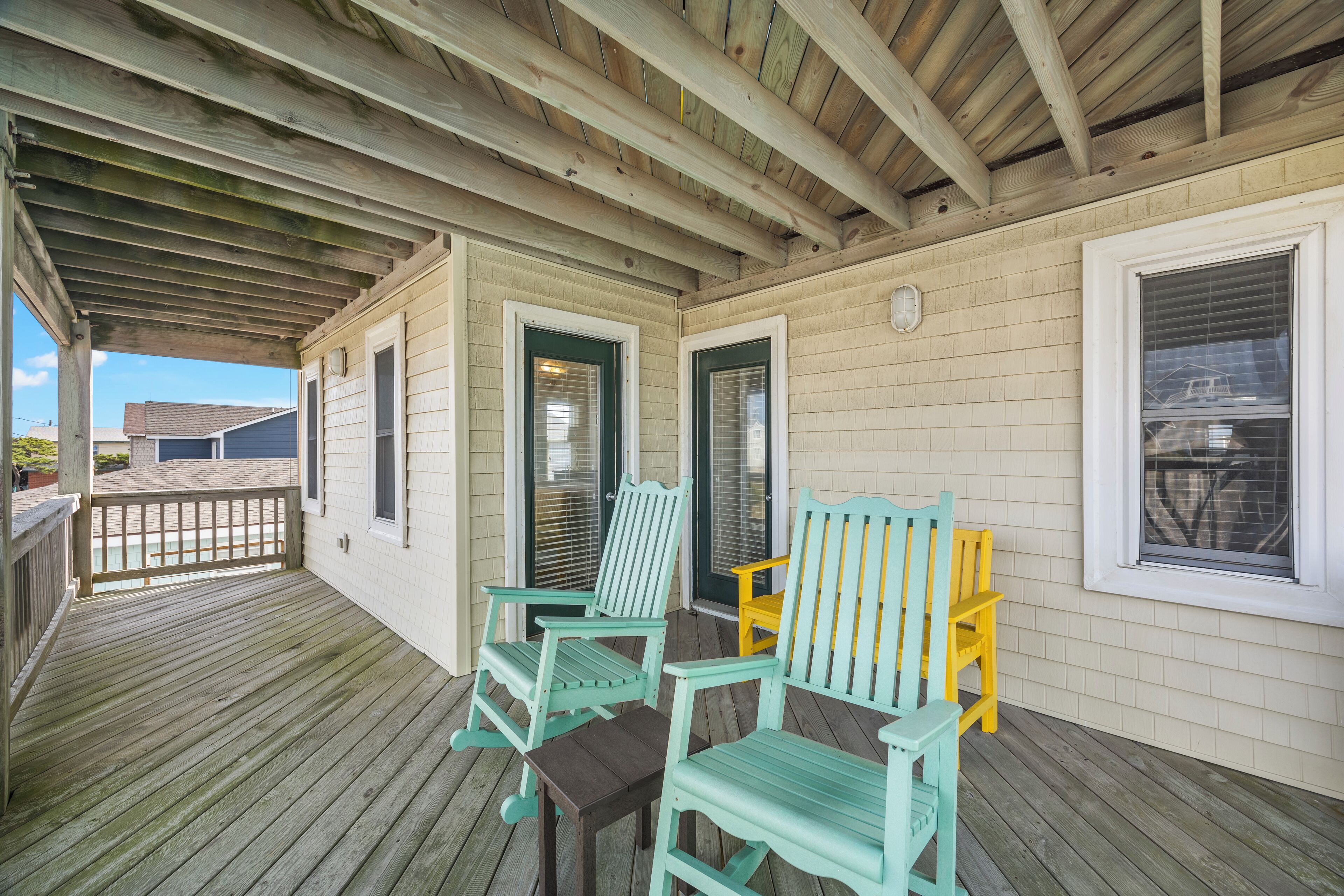 A covered porch with wooden flooring and a wooden ceiling. There are two green Adirondack chairs and a yellow chair.