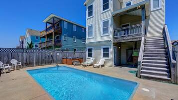 A swimming pool with lounge chairs, a wooden deck, and a multi-story building with balconies.