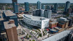 A modern building with a curved facade, surrounded by high-rise buildings and a parking area.