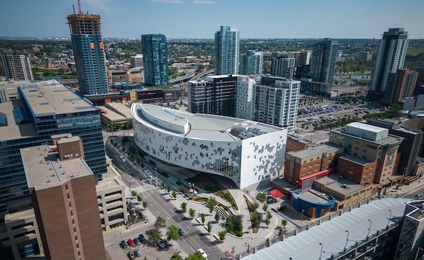 A modern building with a curved facade, surrounded by high-rise buildings and a parking area. - Spacious 3 Beds, Stampede, Saddledome, A/C, Underground Parking (Calgary)
