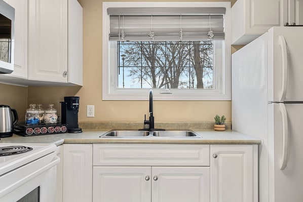 A kitchen with white cabinets, a stainless steel sink, a black faucet, a window with blinds, and a refrigerator. - Spacious 3 Beds, Stampede, Saddledome, A/C, Underground Parking (Calgary)